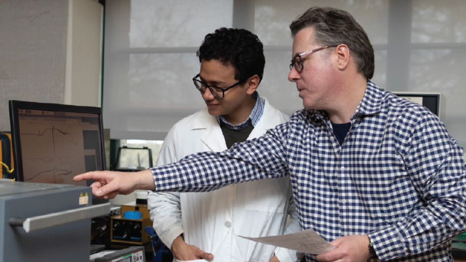 Faculty member and student performing research in front of a computer monitor and equipment