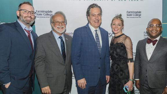 Group of people smiling at the camera in front of a Farmingdale State College branded backdrop